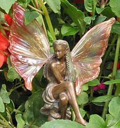 a statue of a fairy sitting on top of a flower pot next to red flowers