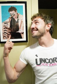 a man pointing to a poster hanging on the wall next to a doorway with his hand up in front of him