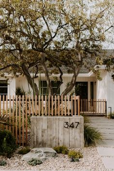 a white house with a wooden fence in front of it and trees on the other side