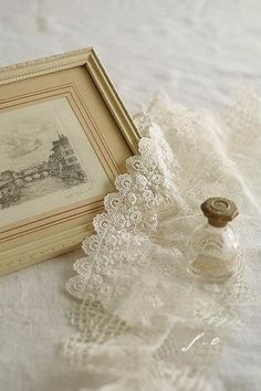 there is a small bottle on the table next to an antique picture frame and lace