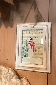 a white frame with a snowman on it hanging from the side of a wall