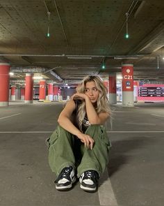 a woman sitting on the ground in an empty parking garage with her hand under her chin