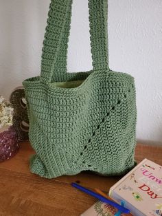 a green crocheted bag sitting on top of a table next to a book