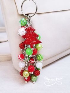 a red christmas tree keychain hanging from a white purse with ornaments on it