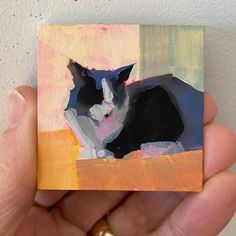 a painting of a black and white cat is being held by someone's hand