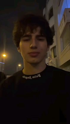 a young man standing in front of a tall building at night with his eyes closed