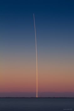 an airplane that is flying in the sky over water at sunset or dawn with a long tail