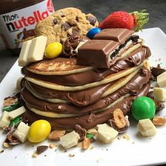 a stack of chocolate covered pancakes on a white plate with candy and cookies around it