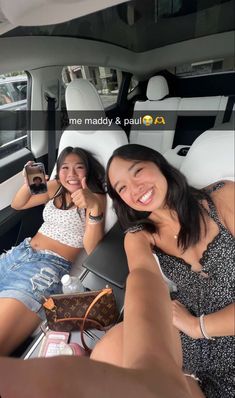 two women sitting in the back of a car taking a selfie with their cell phones