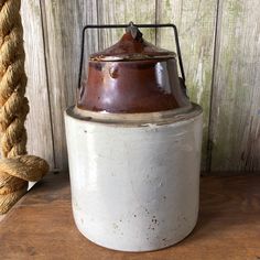 an old white and brown pot sitting on top of a wooden table next to a rope