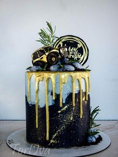 a black and gold cake with yellow drips on it's side, topped with a monster truck