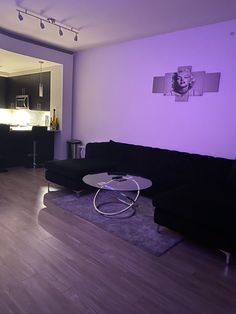 a living room filled with black furniture and purple lighting on the wall above it is a white coffee table