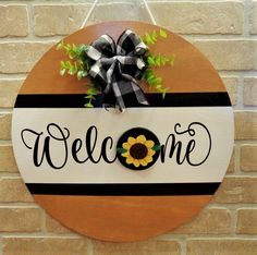 a welcome sign hanging on the side of a brick wall with a sunflower and ribbon