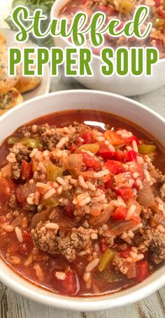 a bowl of stuffed pepper soup on a table with bread and vegetables in the background