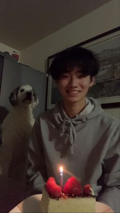 a man standing in front of a white cake with strawberries on it and a dog behind him