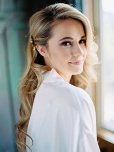 a woman with long blonde hair wearing a white shirt and looking into the distance while standing in front of a window