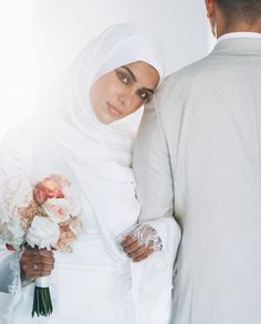 a man and woman dressed in white standing next to each other with flowers on their wedding day