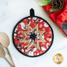 a wooden spoon rest next to a christmas ornament on a white table with red and black wrapping