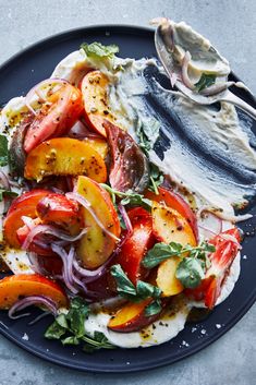 a black plate topped with sliced peaches, onions and feta cheese covered in herbs