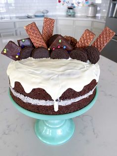 a chocolate cake with white frosting and cookies on top sitting on a blue pedestal