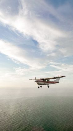 an airplane flying over the ocean on a sunny day with clouds in the sky above