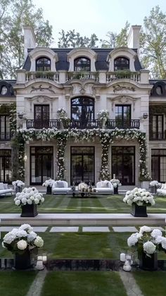 a large house with white flowers in front of it and lawn area next to it