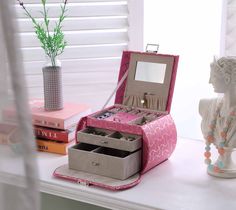 an open pink jewelry box sitting on top of a white table next to a vase with flowers