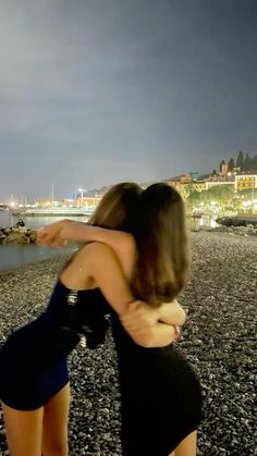 two women hugging each other on the beach at night with city lights in the background