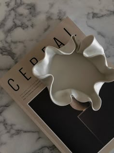 a book with a white bowl on top of it next to a marble countertop