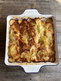 a casserole dish with potatoes and cheese on top, sitting on a wooden table