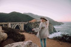 a woman standing on top of a hill next to the ocean with a bridge in the background