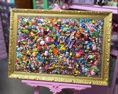 a large group of toy figurines are displayed in a gold frame on a pink stand