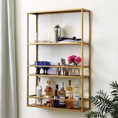 a gold shelf with liquor bottles and glasses on it next to a potted plant