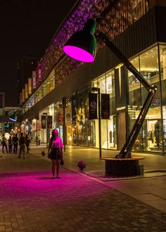 a woman is walking down the street in front of a building with lights on it