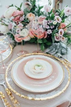 the table is set with pink and white plates, gold rimmed glasses, and floral centerpieces