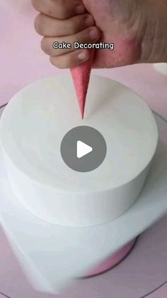 someone is decorating a white cake with pink icing on the top and bottom