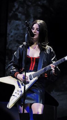 a woman holding a guitar while standing in front of a microphone