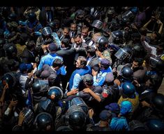 a large group of people surrounded by police helmets and holding hands in the middle of them