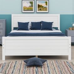 a bedroom with blue walls and white bedding, rugs and two framed pictures on the wall