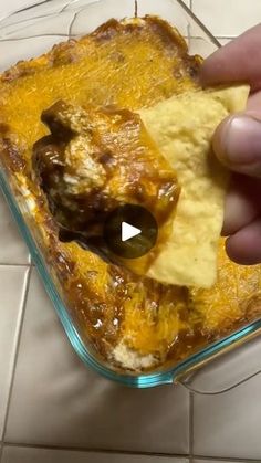 someone is dipping an item into a casserole dish with cheese and tortilla chips