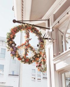 a peace sign made out of flowers hanging from the side of a building in front of a window