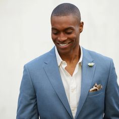 a man in a blue suit smiles as he looks down at his cell phone while wearing a boutonniere