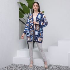 a woman standing in front of a plant wearing a blue crocheted cardigan