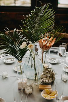 two vases filled with flowers and greenery sit on top of a round table