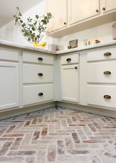 a kitchen with white cabinets and brick flooring in the middle, has a potted plant on the counter