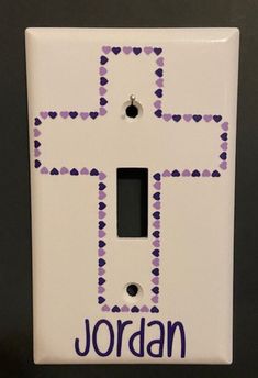 a white light switch cover with a cross painted on it's side and the word jordan written in purple