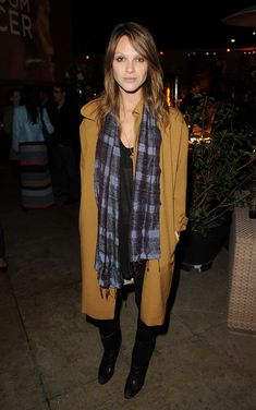 a woman standing in front of a building at night wearing a scarf around her neck