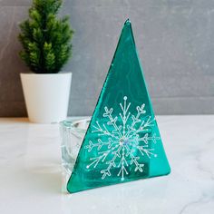 a green glass christmas tree sitting on top of a table next to a potted plant