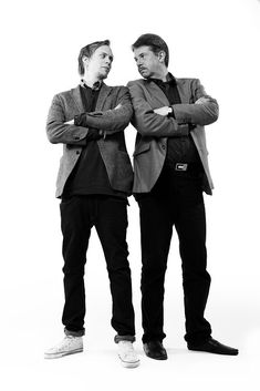 two men standing next to each other in front of a white background with their arms crossed