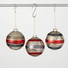 three ornaments hanging from a metal bar on a white wall, one red and one blue striped ornament